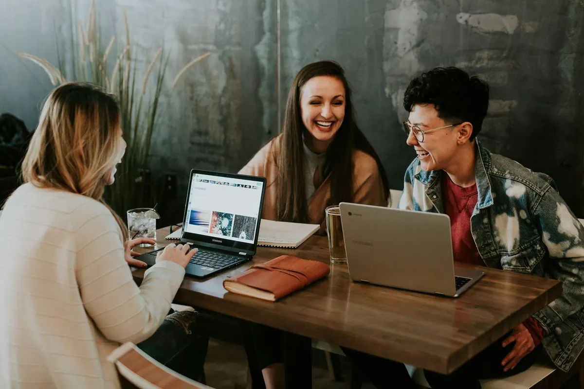 Three students talking around a table with laptops and notebooks
